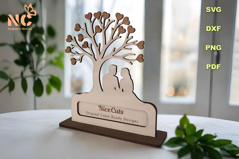 Puede incluir: Corte de madera de una pareja de pie bajo un &aacute;rbol con corazones como hojas. El &aacute;rbol est&aacute; sobre una base con un letrero que dice "Nice Cuts Original Laser Ready Designs".