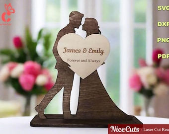 May include: Wooden wedding cake topper featuring a silhouette of a couple embracing, with a heart-shaped insert. The heart is engraved with "James & Emily Forever and Always". The topper is dark brown with a light brown heart.