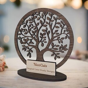 May include: A wooden tree of life design with intricate branches and leaves. The tree is mounted on a wooden base with a small plaque that reads "NiceCuts Original Laser Ready Designs".