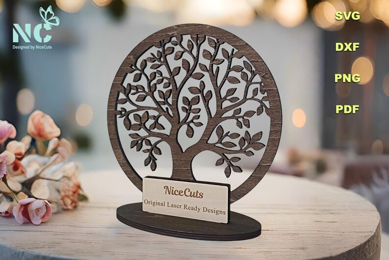 May include: A wooden tree of life design with intricate branches and leaves. The tree is mounted on a wooden base with a small plaque that reads "NiceCuts Original Laser Ready Designs".
