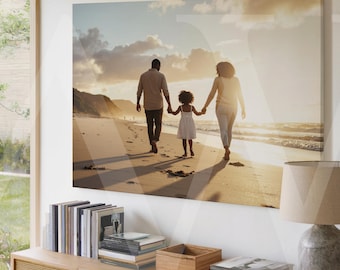 May include: A framed canvas print showing a family of three strolling along a beach at sunset. The parents are holding hands with their child. The print is displayed above a wooden cabinet with books and a lamp.