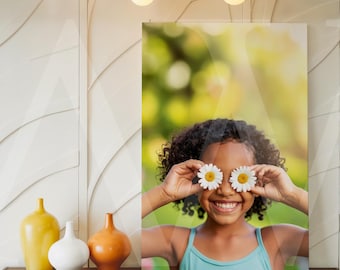 May include: A framed print of a smiling child holding daisies over their eyes. The print is displayed on a wooden console table with decorative vases. A modern light fixture hangs above, against a textured white wall.