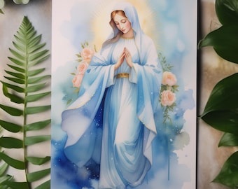 May include: A watercolour print depicting a woman in a blue robe with hands clasped in prayer. The artwork uses a soft palette of blues, whites, and peach, with a golden halo and floral accents. Green foliage surrounds the image.