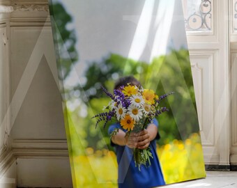 May include: A canvas print depicting a child holding a vibrant bouquet of flowers. The arrangement includes yellow daisies, purple lavender, and orange gerberas. The background shows a blurred field of yellow flowers and green trees.