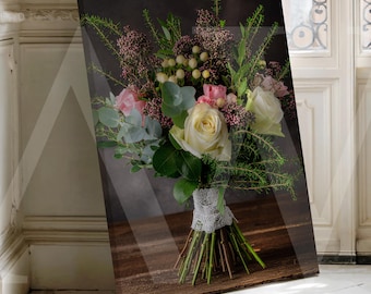 May include: A canvas print of a floral bouquet with white, pink, and yellow roses, greenery, and berries. The stems are tied with lace. The print is set against a dark background and displayed on a wooden surface.