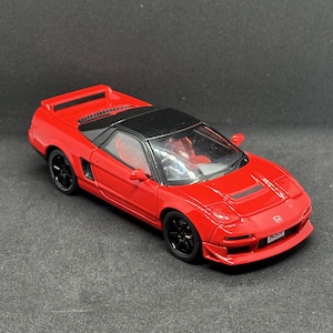 May include: A red Honda NSX scale model car featuring a black roof, black wheels, and a rear spoiler. The vehicle has a detailed interior with red seats, a front bumper air intake, and a license plate with the text NSX clearly visible on the front.