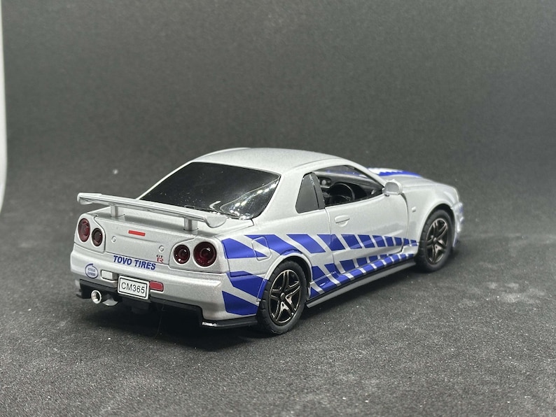 Op de afbeelding: Een witte speelgoedauto met blauwe en zwarte race strepen. De auto heeft een zwarte achter spoiler en de woorden "TOYO TIRES" en "CM385" gedrukt op de achterkant.