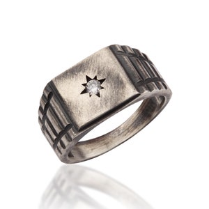 May include: A silver signet ring with a square face and a single diamond set in a star shape. The band has a textured design.