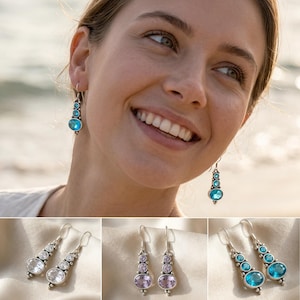 Könnte beinhalten: Silberne Hängeohrringe mit blauen Edelsteinen. Die Ohrringe haben eine Reihe von runden und ovalen blauen Steinen, die einen Kaskadeneffekt erzeugen. Variationen mit klaren und violetten Edelsteinen sind ebenfalls abgebildet.