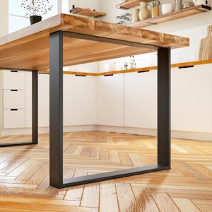 May include: A large wooden dining table with a natural finish, supported by black metal legs. The table is in a bright kitchen with white cabinets and wooden flooring. The table's dimensions are approximately 183 cm long, 91 cm wide, and 76 cm high.