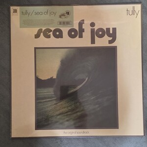 May include: A vinyl record album titled "sea of joy" by Tully. The album cover features a dark image of a wave and the text "sea of joy" in large, bold letters. The words "the original soundtrack" are at the bottom.