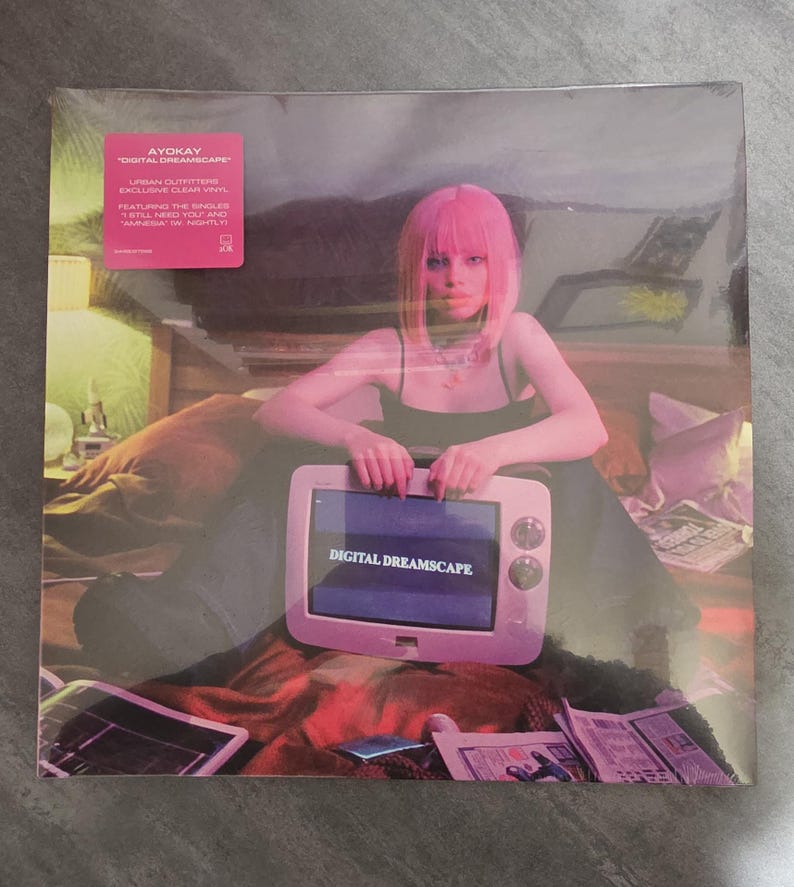 May include: A vinyl record featuring the album "Digital Dreamscape" by Ayokay. The album cover shows a person with pink hair holding a retro-style television with the album title on the screen. The record is in a clear plastic sleeve.
