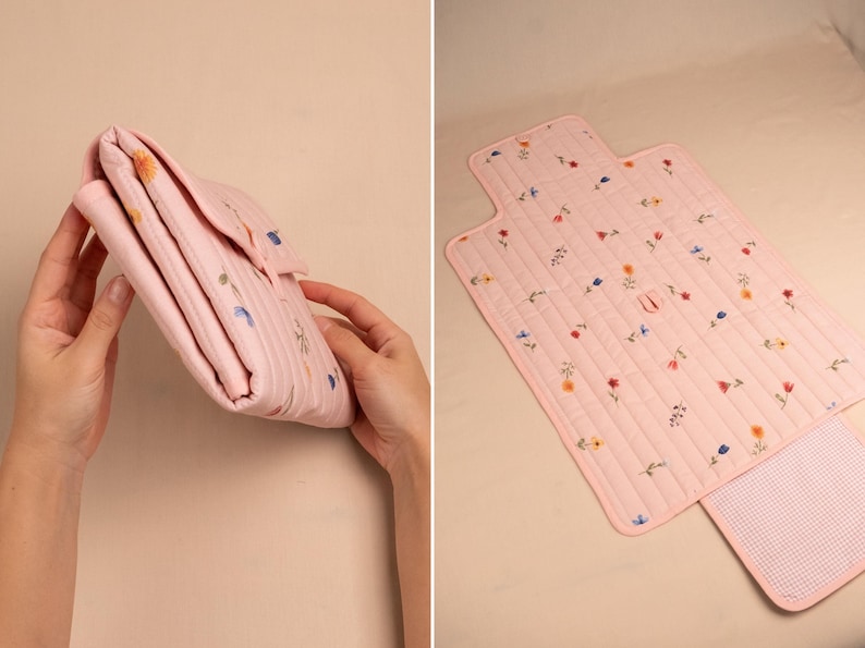 Puede incluir: Un cambiador acolchado rosa con un estampado floral. El cambiador est&aacute; doblado en la primera imagen y desplegado en la segunda, revelando una extensi&oacute;n forrada con cuadros vichy. Est&aacute; decorado con flores bordadas en varios colores.