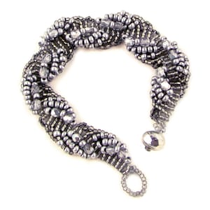 Può includere: Un braccialetto argentato con un design intrecciato. Il braccialetto è realizzato con perline piccole e rotonde e perline più grandi e sfaccettate.