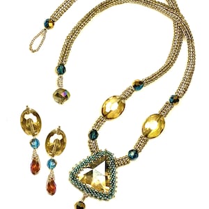 Op de afbeelding: Een gouden kralenketting met een grote driehoekige kristallen hanger en bijpassende oorbellen. De hanger heeft een kleiner kristal in het midden en is omgeven door kleinere kralen. De oorbellen zijn eenvoudig en hebben een enkel kristal.