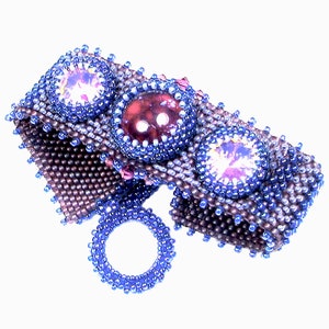 Pode incluir: Um bracelete de contas com três pedras preciosas grandes e facetadas. O bracelete é feito de contas marrons e azuis e tem um fecho de anel.