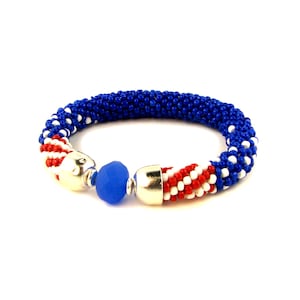 May include: A blue, white, and red beaded bracelet with silver clasps and a blue glass bead.