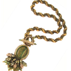 Op de afbeelding: Een groene en bruine kralenketting met een groene stenen hanger en bladaccenten.