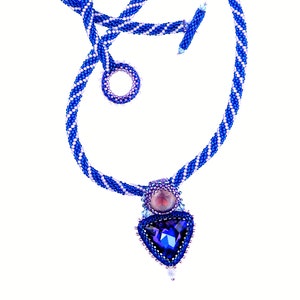 May include: A blue and white beaded necklace with a triangular pendant featuring a large blue gemstone and smaller purple and blue gemstones.