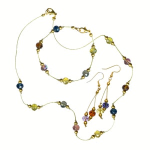 May include: A gold-toned jewelry set featuring a necklace, bracelet, and earrings. The necklace and bracelet are strung with colorful, faceted beads in shades of blue, yellow, purple, and brown. The earrings have dangling beads.