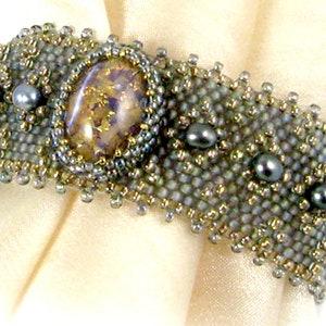 May include: A beaded bracelet featuring a large iridescent gemstone at its centre, surrounded by smaller grey beads. The bracelet is crafted with a mix of grey and gold beads.