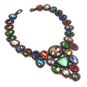 Può includere: Una collana di perline colorate con un ciondolo a forma di lacrima che presenta una varietà di pietre preziose, tra cui turchese, smeraldo e rubino.