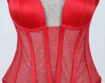May include: A red satin and mesh corset with a sweetheart neckline and boning. The corset has a sheer mesh panel in the front and is lined with satin.