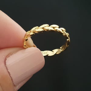 May include: A gold ring with a leaf design. The ring is made of gold and features a repeating pattern of leaves around the band. The ring is held up by a person's fingers. The ring has the number "585" engraved on it.