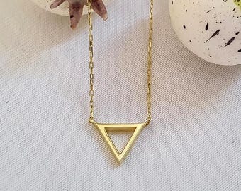 May include: A gold-colored necklace featuring a delicate chain and a geometric triangle pendant. The pendant is a simple, open-frame design. The necklace is displayed on a white surface.