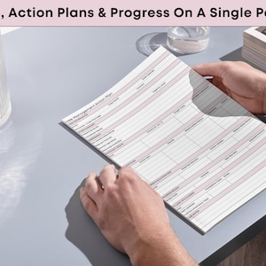 May include: A person holding a Time Management Action Plan. The document has a pink header and pink lines. The text "Goals, Action Plans & Progress On A Single Page" is at the top. A glass and a small dish are in the background.