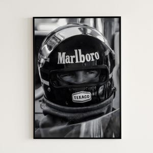 Peut inclure: Photographie en noir et blanc d'un pilote de course portant un casque noir avec un logo "Marlboro" blanc et un logo "Texaco" blanc. Le pilote regarde sur le côté.