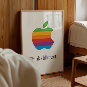 May include: Framed poster featuring the iconic Apple logo in a rainbow design, with the words "Think different" below. The poster is in a wooden frame and leans against a wooden wall.