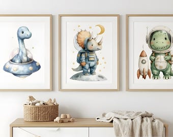 May include: Three framed watercolor prints featuring adorable dinosaurs. One shows a blue dinosaur in a UFO, another a triceratops in a spacesuit, and the last a dinosaur astronaut with a rocket. The prints are in light wood frames.
