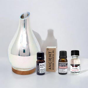 May include: A white iridescent glass diffuser with a wooden base, three essential oil bottles, and three labels that read "Happiness", "Ancient Wisdom - Essential Oil", and "Vanilla Fragrance Oil".