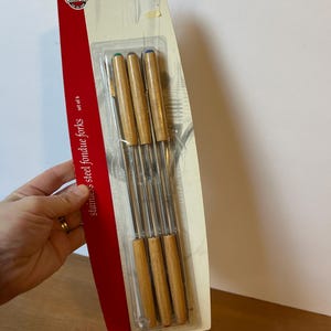 May include: A package of six stainless steel fondue forks. Each fork has a wooden handle and a colored tip. The packaging is white and red, with the brand name "NORPRO" visible. The forks are approximately 9.5 inches / 24 cm long.