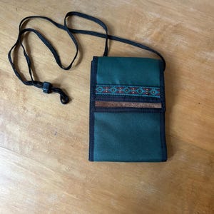 May include: A dark green fabric crossbody bag with a black strap and a brown leather accent. The bag has a geometric pattern in blue, red, and white.