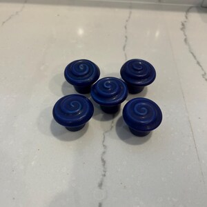 May include: A set of five dark blue cabinet knobs, each featuring a raised, circular spiral pattern on the top surface. The knobs have a smooth, rounded shape and a uniform, deep blue color throughout their construction.