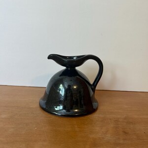 May include: A small, dark blue ceramic creamer with a handle and a spout. The creamer has a bell-shaped base and a smooth, glossy finish. The handle is curved, and the spout is small and pointed.