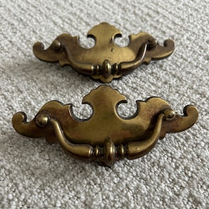 May include: A white ceramic mug with a black handle and the text "But First, Coffee" in a black, handwritten-style font. The mug is on a white surface.