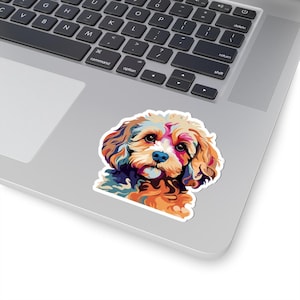 Op de afbeelding: Een kleurrijke sticker met een gestileerde illustratie van een hondengezicht. Het kunstwerk maakt gebruik van een levendig palet van oranje, blauw, geel en paars. De sticker is op een laptop geplaatst.