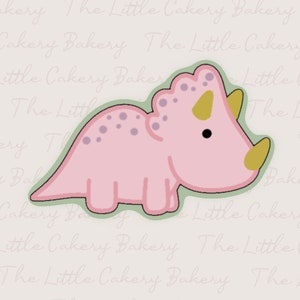 Op de afbeelding: Roze triceratops koekjesvormer met een groene omtrek. De koekjesvormer heeft een gele hoorn en paarse stippen.