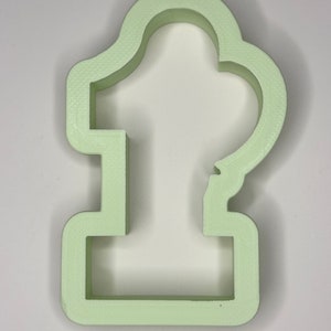 May include: A light green plastic cookie cutter shaped like the number one. The cutter has a rounded top and a flat base.