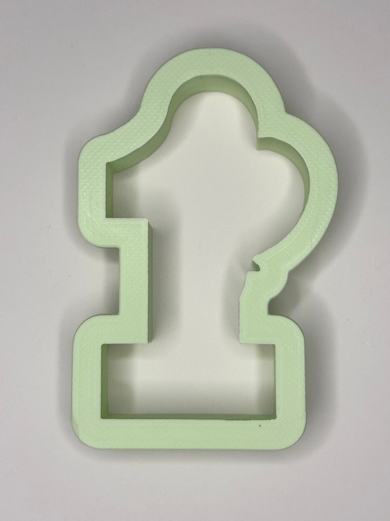May include: A light green plastic cookie cutter shaped like the number one. The cutter has a rounded top and a flat base.