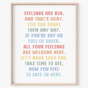 May include: A framed print with the text "FEELINGS ARE BIG, AND THAT'S OKAY. YOU CAN SHARE THEM ANY DAY. IF YOU'RE SHY OR FULL OF CHEER. ALL YOUR FEELINGS ARE WELCOME HERE. LET'S NAME EACH ONE. TAKE TIME TO SEE, HOW YOU FEEL IS SAFE IN HERE." The text is in rainbow colors.