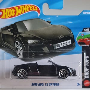 Puede incluir: Un coche de juguete descapotable negro Audi R8 Spyder 2019 en una tarjeta Hot Wheels azul y blanca. El coche tiene llantas plateadas y el texto "R8 Spyder" en la matrícula. La tarjeta también presenta el logotipo de Hot Wheels y el texto "DROP TOPS".