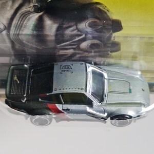Może przedstawiać: Srebrno-czarny samochodzik z czerwono-białymi akcentami. Samoch&oacute;d ma napis "PORSCHE" z boku. Miniaturowa replika samochodu sportowego.