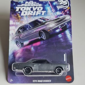 May include: A silver 1970 Road Runner die-cast car from the Hot Wheels Silver Series, part of the Fast & Furious: Tokyo Drift collection. The packaging features a cityscape background and the text "25 Years of Fast & Furious".