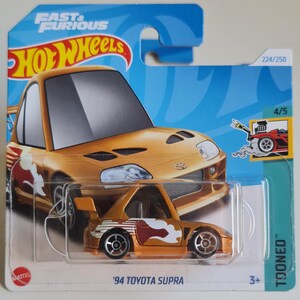 May include: A gold-coloured '94 Toyota Supra toy car from the Fast & Furious series, packaged on a blue and white card. The car features a flame design and is part of the Hot Wheels collection.