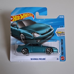 May include: A teal 1998 Honda Prelude die-cast toy car in its original blue and white Hot Wheels blister packaging. The card features the text '98 HONDA PRELUDE', 'FACTORY FRESH', and '136/250'. The car has silver wheels and a metallic finish.