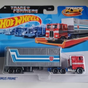 May include: A Hot Wheels Optimus Prime toy truck on a blue and white card. The truck is red and blue with a silver trailer. The card features the Hot Wheels and Transformers logos.